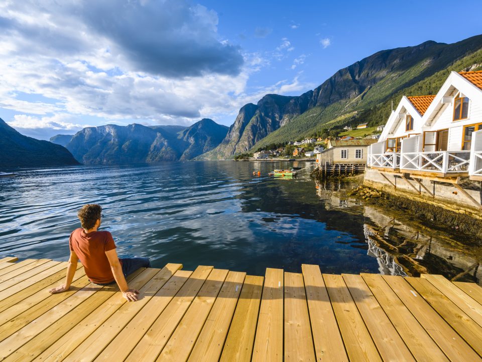 Man-sitting-on-wooden-pier-admiring-a-Norwegian-Fjord-Western-Norway