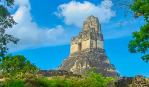 Maya Ruine met blauwe lucht, omringd door boombladeren
